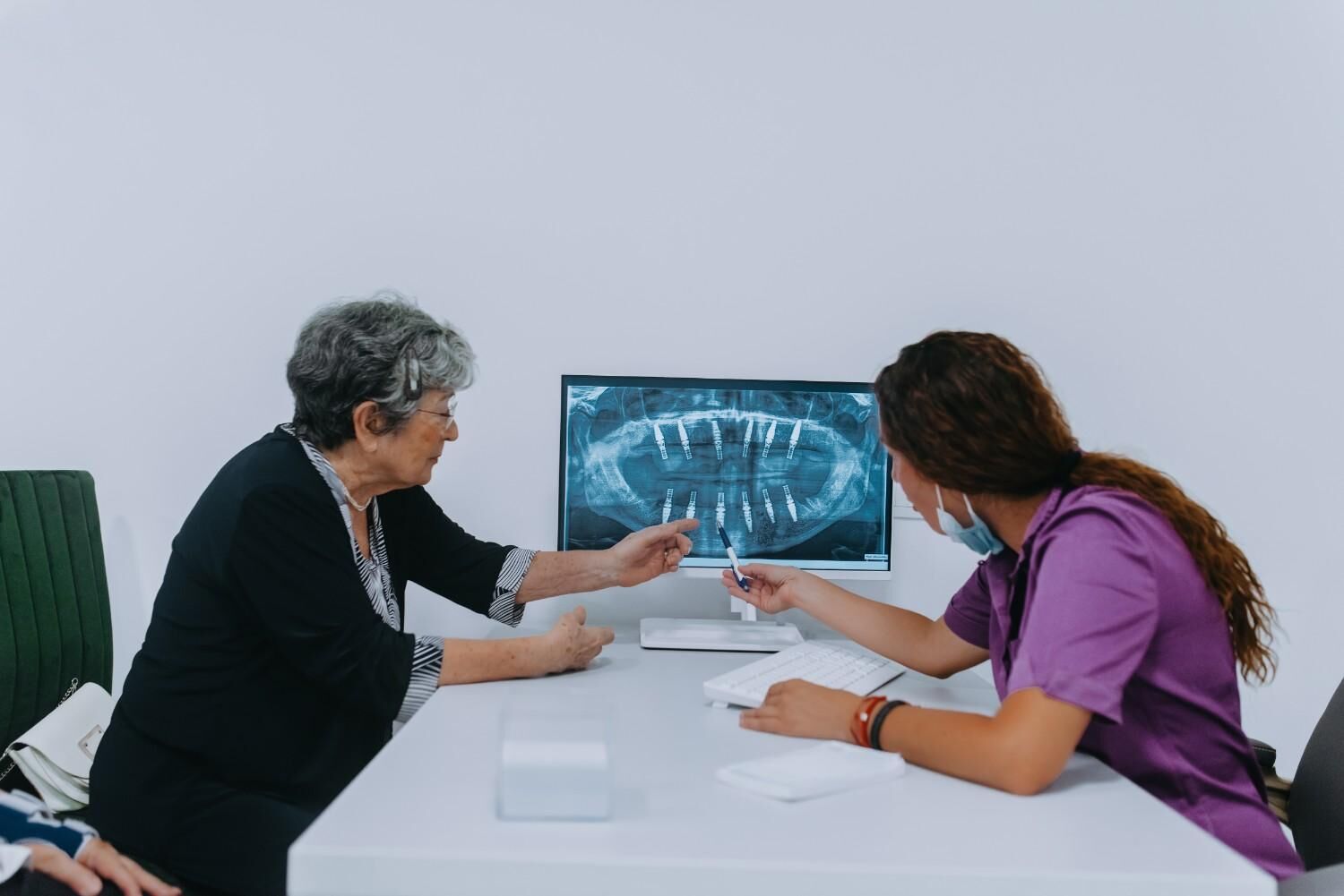 An older woman and a dental professional review a dental X-ray with implants displayed on a computer screen.
